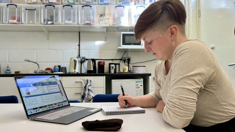 A Collections Assistant writes in a notepad in front of an open laptop