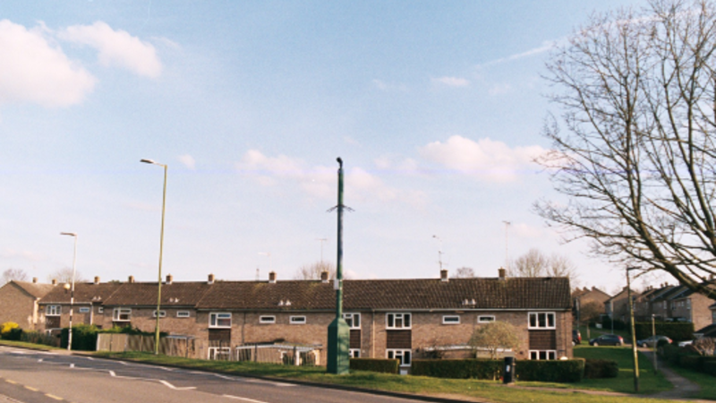 Photograph of a moving surveillance camera within a council estate in Letchworth Garden City. Colour photograph, with a blue, slightly cloudy sky behind.