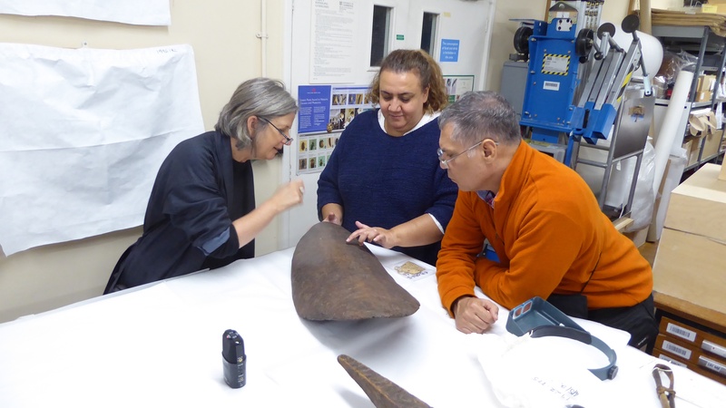 Three people study an object around a table.