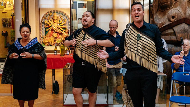 Two men and a woman, dressed in traditional pacific dress, perform in the MAA gallery.