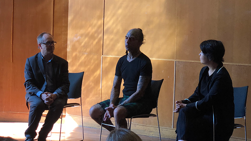 Three people sitting and talking on a stage, with microphones.