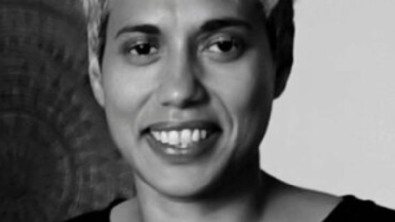 A curator smiles into the camera. The image is black and white and she has short light coloured hair and wears a dark top.