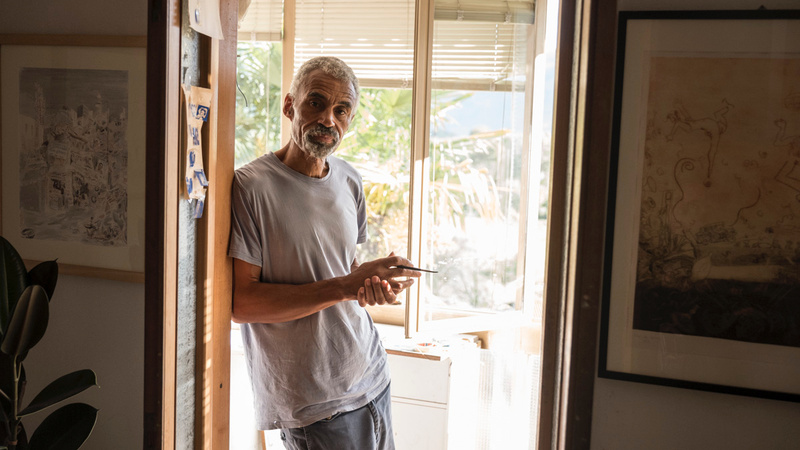 Tony Phillips standing in the doorway of his home studio in Italy, holding a paintbrush.