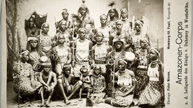a photograph of a group of women from the Dahomey region with a caption that says “Amazonen-Corps a.d. Leibgarde des Konigs v. Dahomey in west Afrika”. 