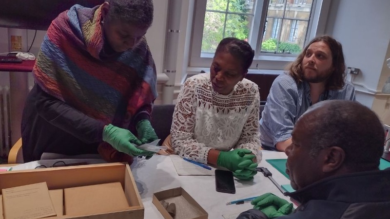 Researchers sit around a table looking at Caribbean artefacts from a box to the left of the image.