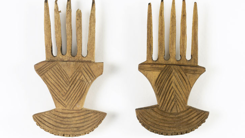  Small wooden comb with five prongs and handle decorated on one side. The handle is fan shaped at the end with a denticulated edges and has incised lines on one side only. 