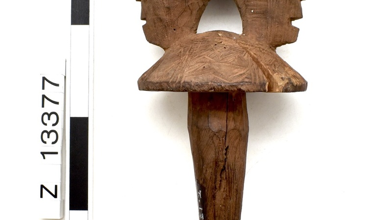 Bottle stopper in a light brown wood. Two back to back heads above, with a large crack running along the length of the object on one side.