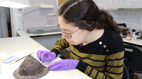 A conservator wearing purple gloves carries out work on a corroded shield boss.