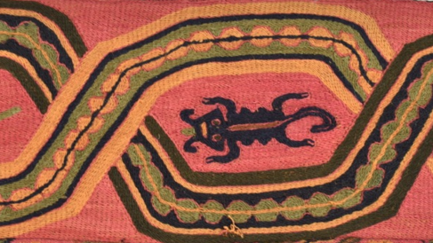  A long, mulitcoloured embroidered band with fringe from the border of a mantle. Background fabric a salmon pink, embroidered with a variety of composite animal figures, which have snake, cat, bird and lizard characteristics.