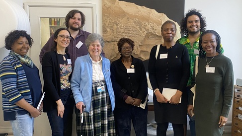 The From Caribbean to Cambridge advisory group stand in the museum's archaeology workroom, smiling broadly. Alongside them is the World Archaeology curator and an honorary affiliated researcher.