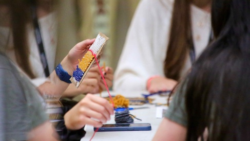Young people create a woven design on a small cardboard loom using brightly coloured wool.
