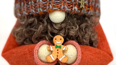 A gnome wearing a knitted hat pulled down over its eyes holds out a gingerbread man.