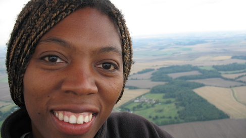 An academic smiles at the camera. Behind her is a view of fields from above.