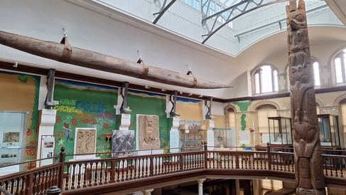 The galleries with sunlight streaming through the glass ceiling. At one end a totem pole rises from the 1st floor through the 2nd floor until it nearly touches the glass overhead. 