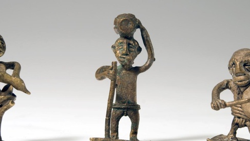 Three Akan goldweights from Ghana, gold in colour and depicting men in various activities, photographed against a grey studio background.