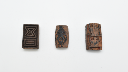 Three body stamps in a horizontal row. L-R: a rectangular stamp with geometric raised relief, in a rectangle and hourglass shape; a rounded stamp with raised relief of a human figure, the raised part black from ink; a rectangular stamp with raised reliefs