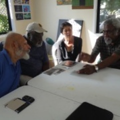 A group of four people sit around a table looking at copies of photographs and pages from a journal.