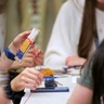 Young people create a woven design on a small cardboard loom using brightly coloured wool.