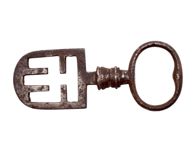 A metal key with an oval bow at one end, a short baluster-like stem, and a symmetrical openwork spade-shaped bit with four internal wards at the other end.