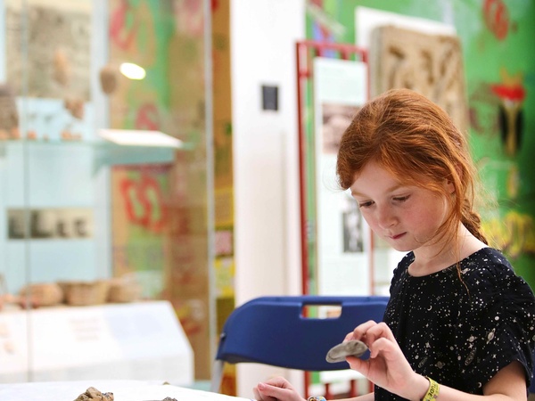 A girl sits at a table in the museum gallery handling pieces of pottery from the Teaching Collection.