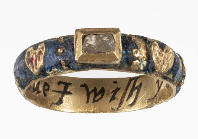 A ring decorated with a small rectangular stone and hearts on the surface of the band. The inside of the band features an inscription.
