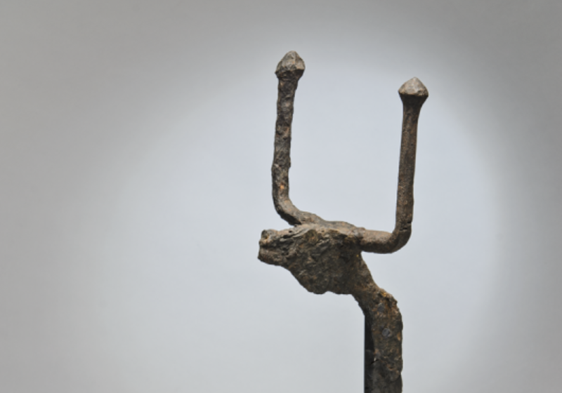 Detail of a bronze horned animal head at the top of a firedog, against a grey studio background.