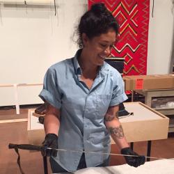 Ayesha Fuentes in a conservation room, wearing black gloves and holding a spear