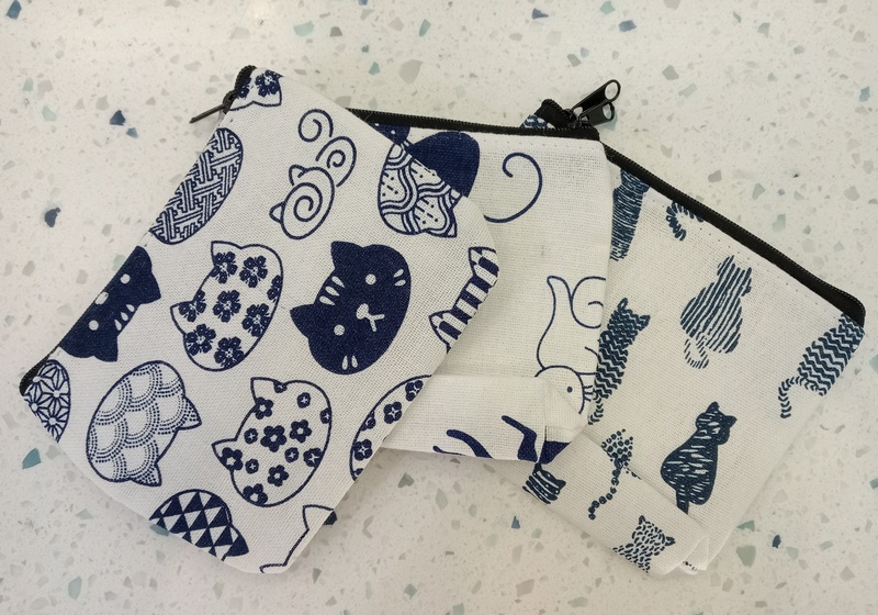 Three small white purses each decorated with a different cat pattern. The top purse features reoccurring cat faces with a range of designs.