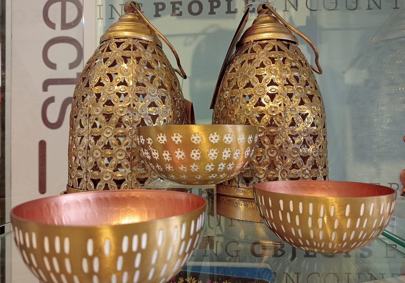 Three brass bowls in front of two lanterns. The lanterns have a floral design cut into them.
