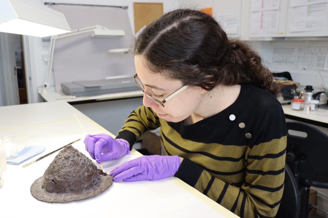 A conservator wearing purple gloves carries out work on a corroded shield boss.