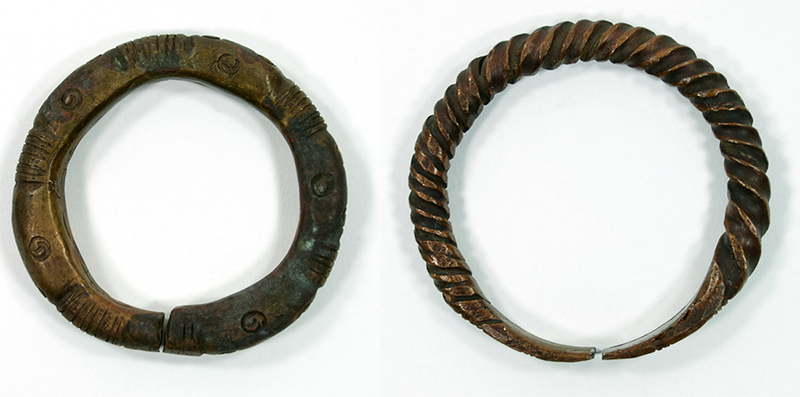 Two bracelets. One is rounded and open, with patterns of spiral and vertical groups of incisions; the other has a twisted design and flat ends.
