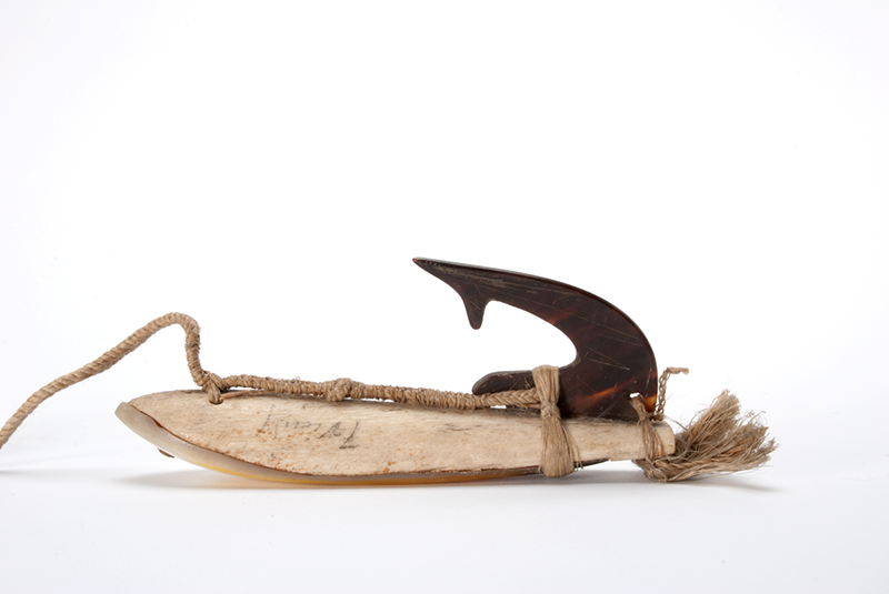Fish-hook carved from a piece of whale shell, with a very dark hook attached, and attached to a cord.
