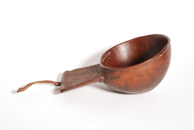 Cup that resembles a coconut cup, with a wide and slightly triangular handle carved with bands of zigzags. A cord is attached.