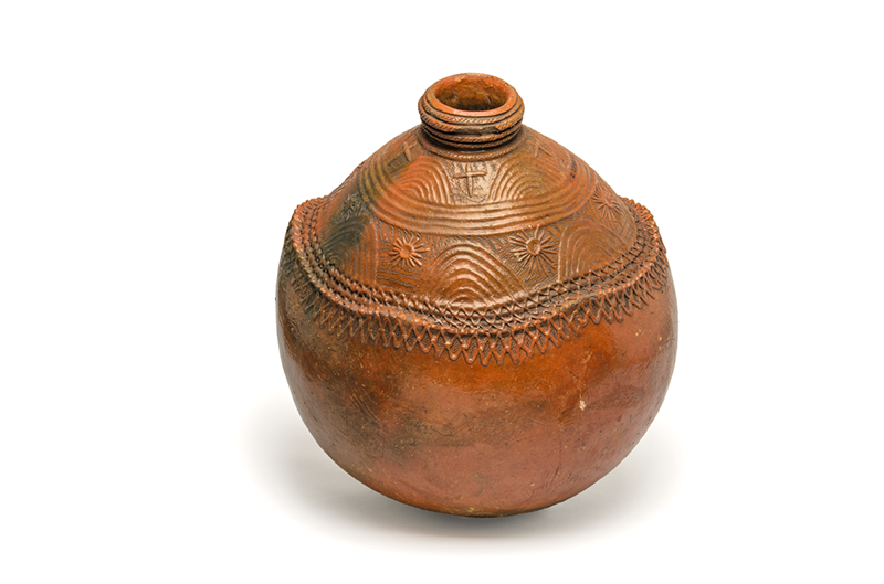 Large water jug, mid orange-brown in colour, glazed ceramic. The upper panel is decorated with 'rainbow' and 'cross' patterns, with the lower panel decorated with rainbow and sun patterns. 