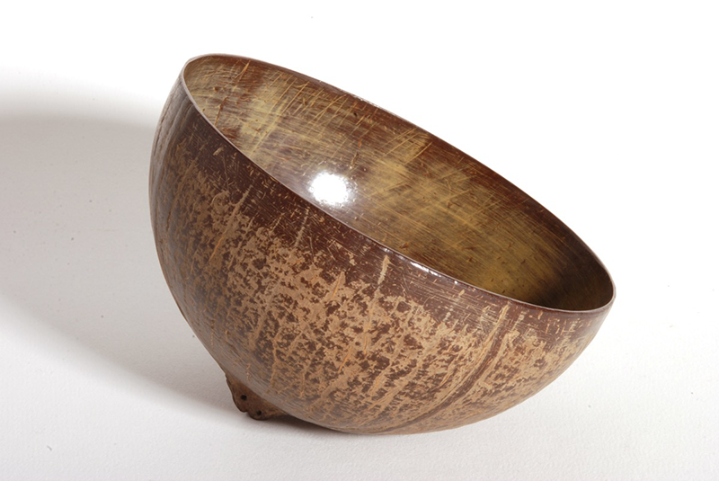 Drinking cup made out of half a coconut shell, with a polished smooth interior and bright yellow patina in places.