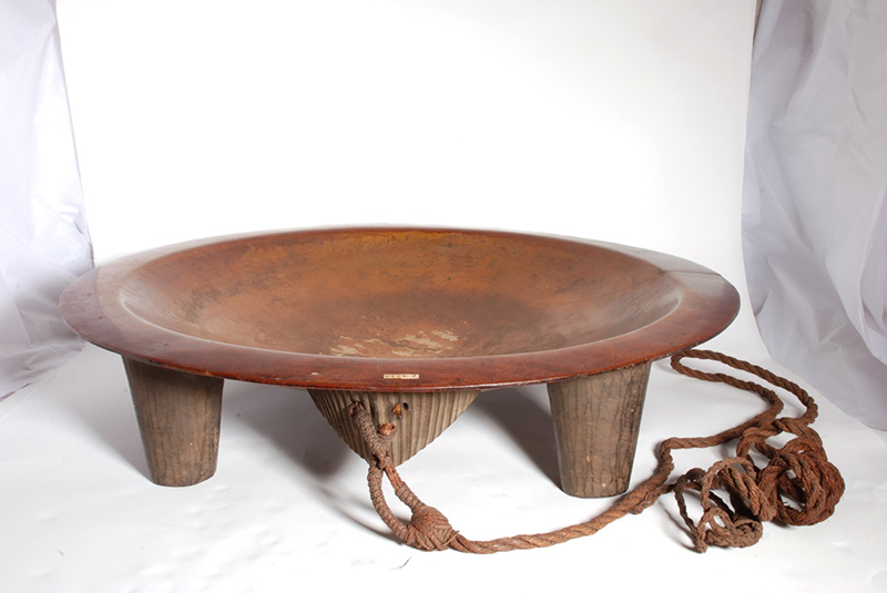 Brown shallow bowl with two legs and a central triangular strainer beneath, with cord hanging down, photographed against a white studio backdrop