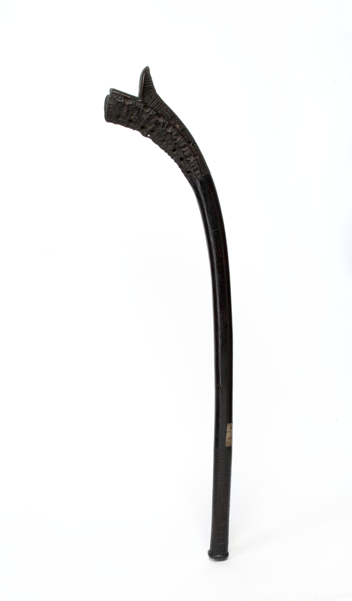 Dark wooden club. The head is triangular, and the handle is curved, with tavatava patterns all over.