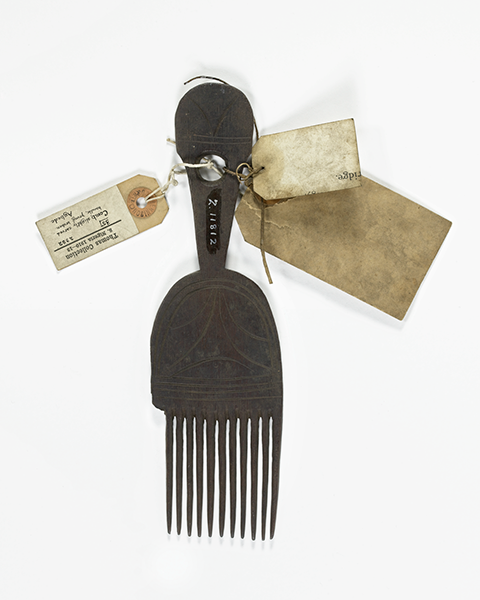 Dark brown wooden comb with slightly carved handle, one prong broken. Three description tags are attached.