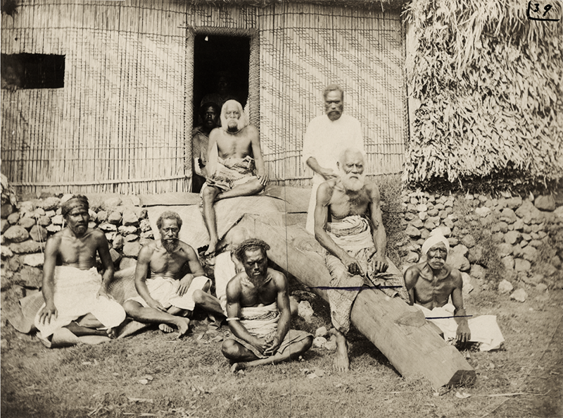 Sepia photograph of a group of Fijian men sitting outside a house