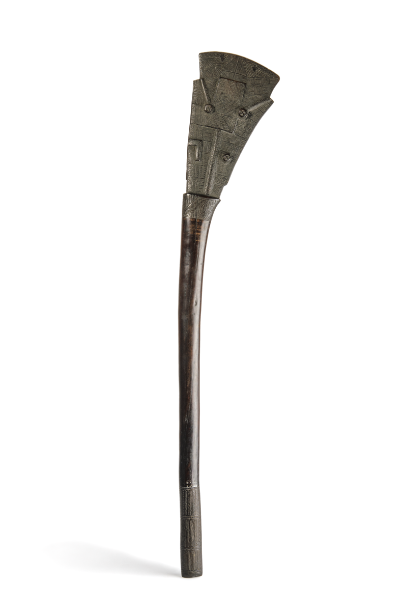 A dark wood club with a thick oval shaft and a triangular shaped head, carved with very fine patterns. 