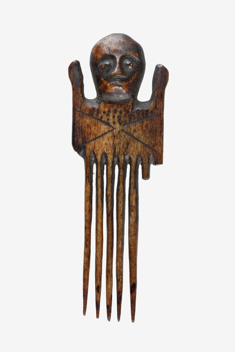 A bone comb originally with eight prongs and a single-sided decorated handle. There is a human head carved at the top of the handle.
