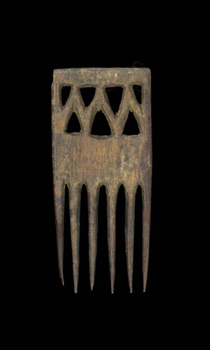 A comb carved from wood with six cylindrical and tapering prongs. The rectangular handle is decorated with a row of four triangular cut-outs with three triangular cut-outs below.