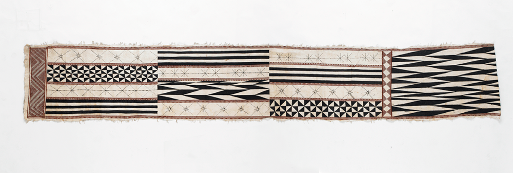  Long piece of barkcloth of which the designs are organised in four rows of rectangles with stencilled designs in red and black. The long edges are fringed