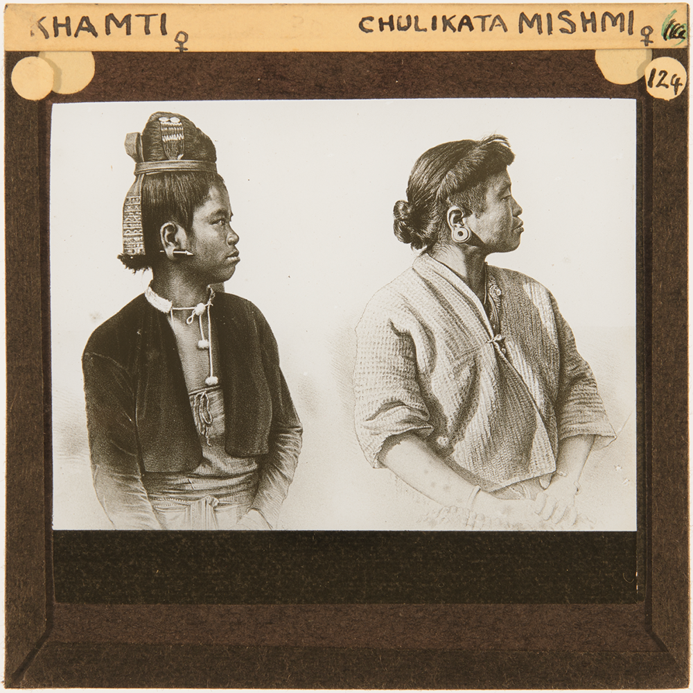 Lantern slide sepia image of two people side by side, in profile view. One is a woman, sat proudly, with her hair tied back with a large ear stretcher and wrap over top, the other a man with an open shirt and ceremonial head/hair wear.