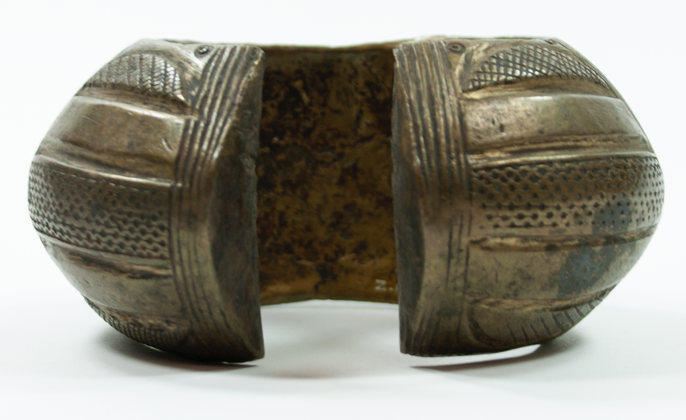  Wrought brass bracelet. Open, with outer edge covered with incised decoration of vertical and horizontal lines