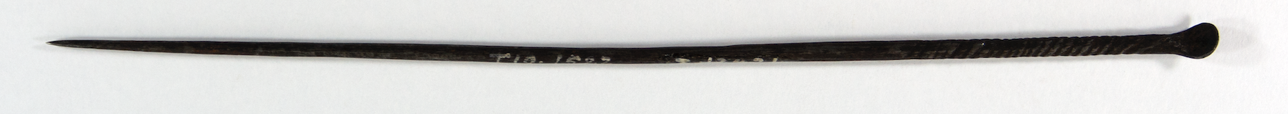 Long cylindrical rod of possibly iron. The head of the pin has been flattened into a small disc like shape, and the other end tapers to a very sharp point.