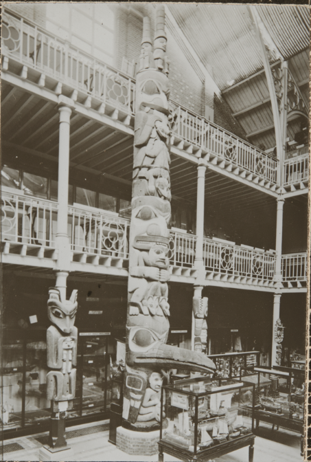 A black and white internal photograph of the Pitt Rivers Museum featuring a totem pole.