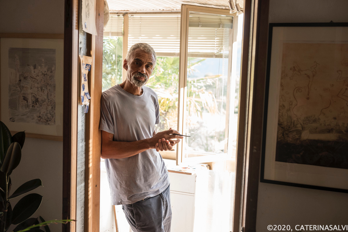 Tony Phillips standing in the doorway of his home studio in Italy, holding a paintbrush.