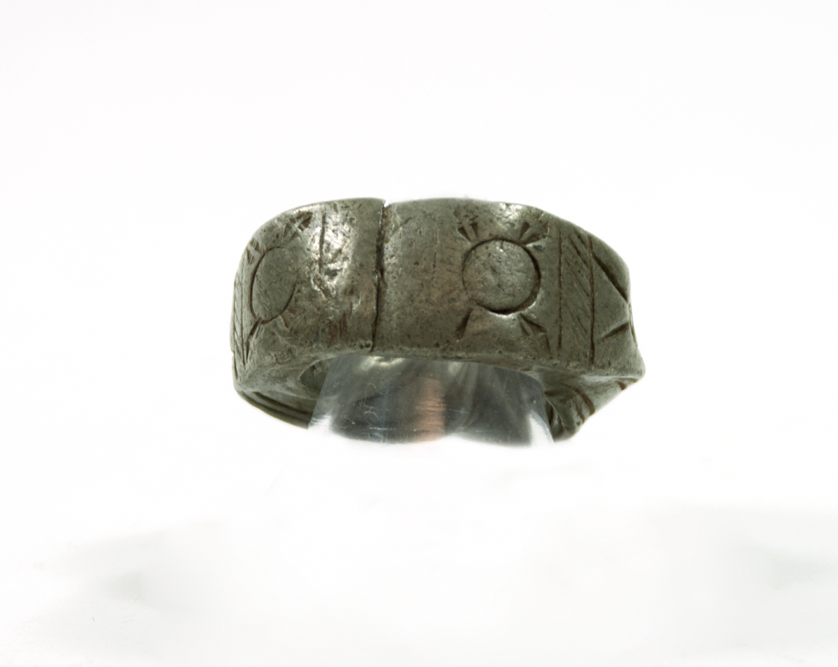 A ring of white metal, twisted with flattened and fused ends. The twists are decorated with lines and the ends with geometric designs.