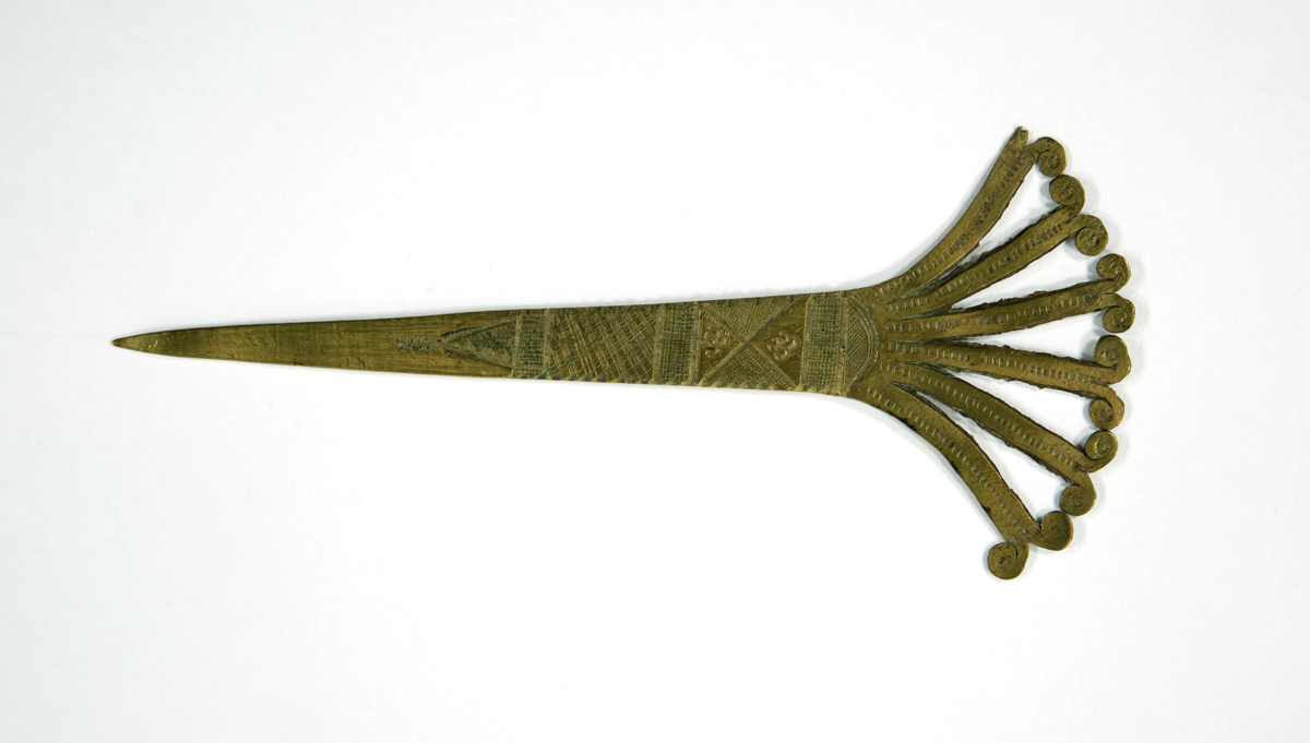  A brass hair ornament or pin. There are six 'branches' that fan out from a flat base to form the head of the pin. Each branch has two spiral ends, making 11 in total as one has broken off. 